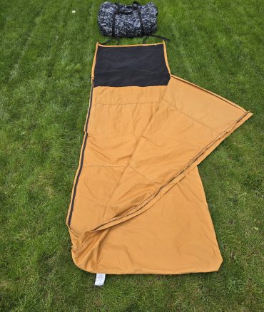 Tan Butler Bedroll folded at an angle with black hood on grass